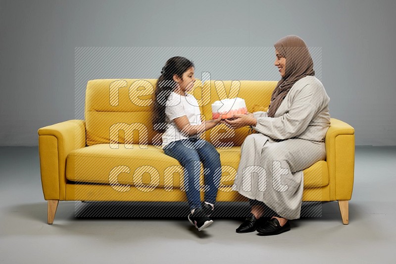 A girl sitting giving a cake to her mother on gray background