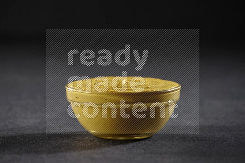 A glass bowl full of mustard paste on black flooring in different angles