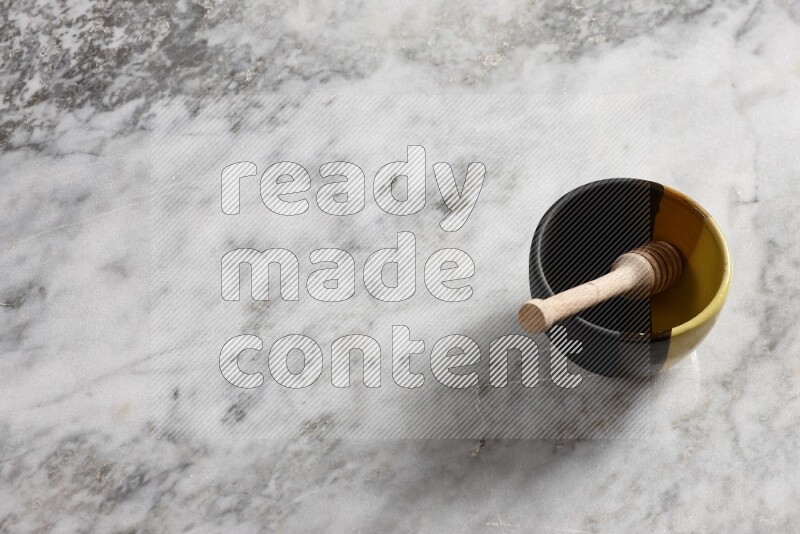 Multicolored pottery bowl with wooden honey dipper in it on grey marble background