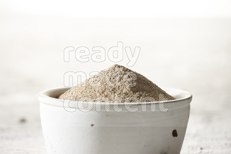 white pottery bowl full of white pepper powder on textured white flooring
