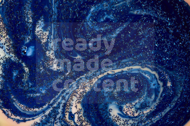 A close-up of sparkling blue glitter scattered on swirling blue and orange background