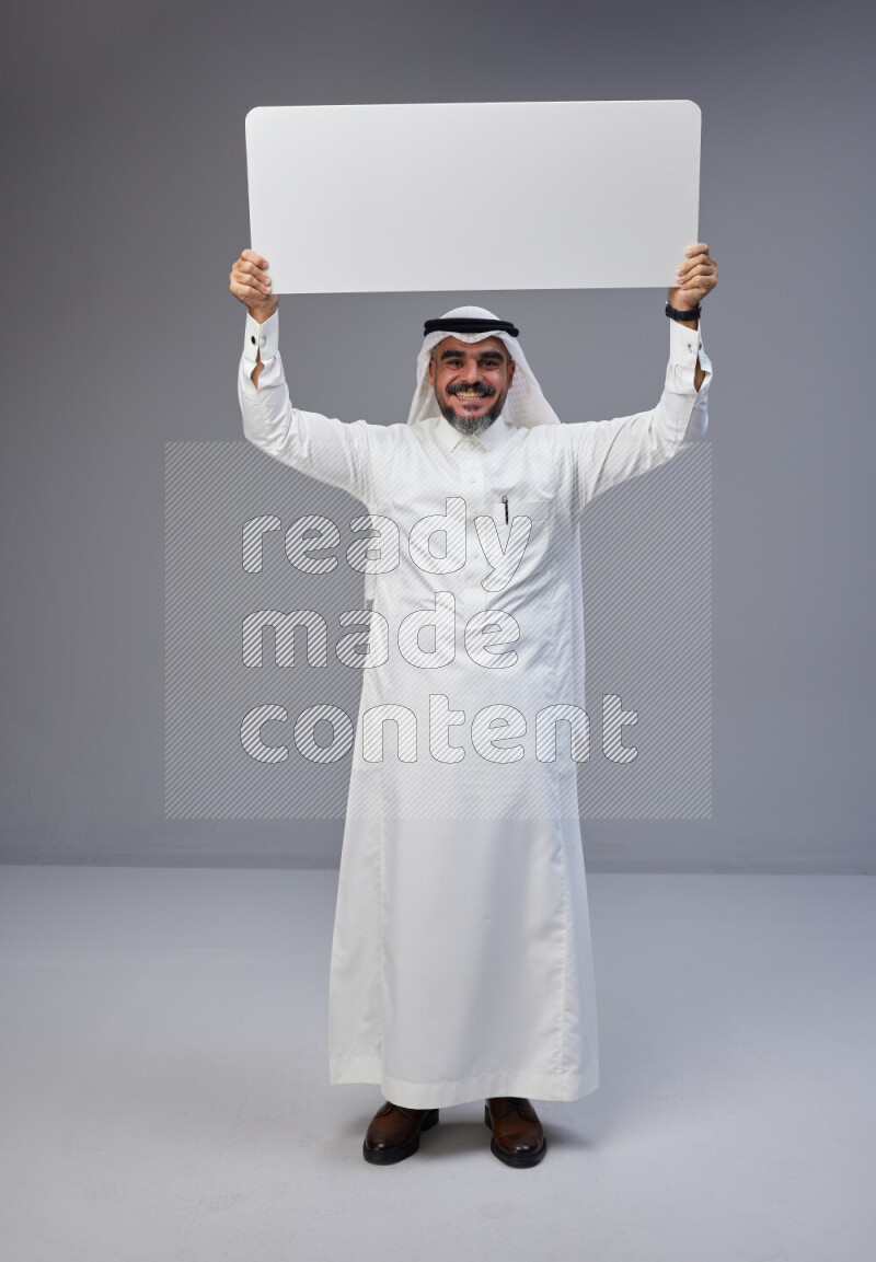 Saudi man Wearing Thob and white Shomag standing holding board on Gray background