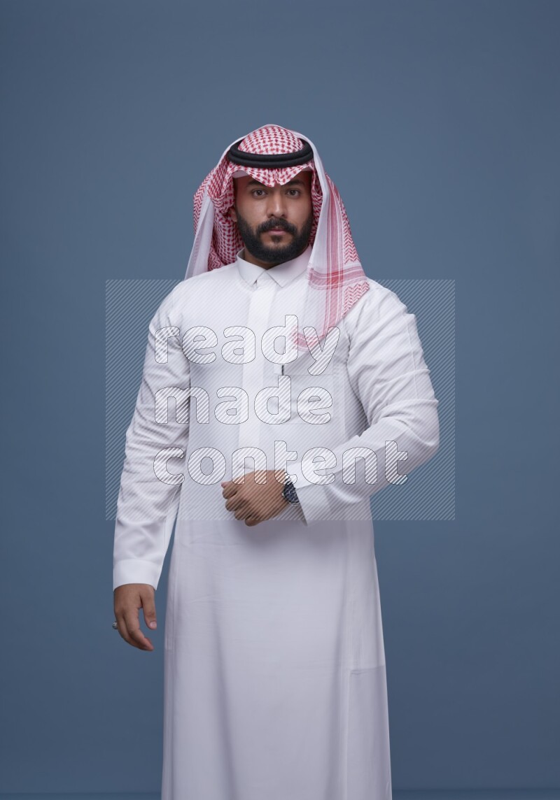 A Saudi man posing on blue background wearing Thob and Shomag