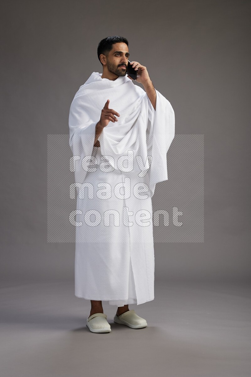 A man wearing Ehram Standing talking on phone on gray background