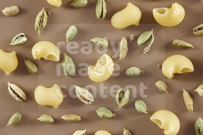 Raw pasta with different ingredients such as cherry tomatoes, garlic, onions, red chilis, black pepper, white pepper, bay laurel leaves, rosemary and cardamom on beige background