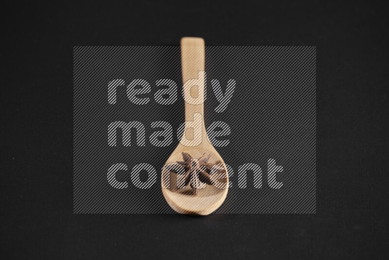 Star Anise in a wooden spoon on more stars anise filling the frame on black flooring