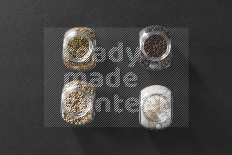 ملح وفلفل أسود وفلفل أبيض وكمون في أوعية زجاجية علي خلفية سوداء