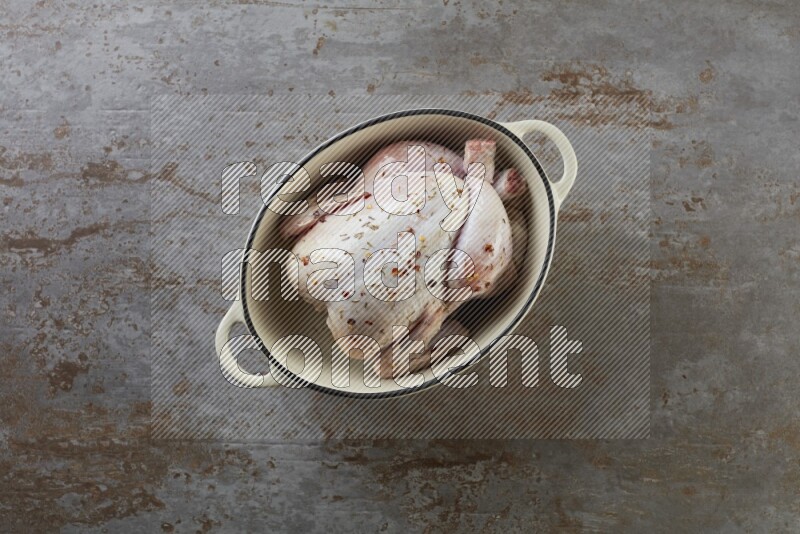 whole raw chicken on in a white ceramic pot direct on a rustic grey background