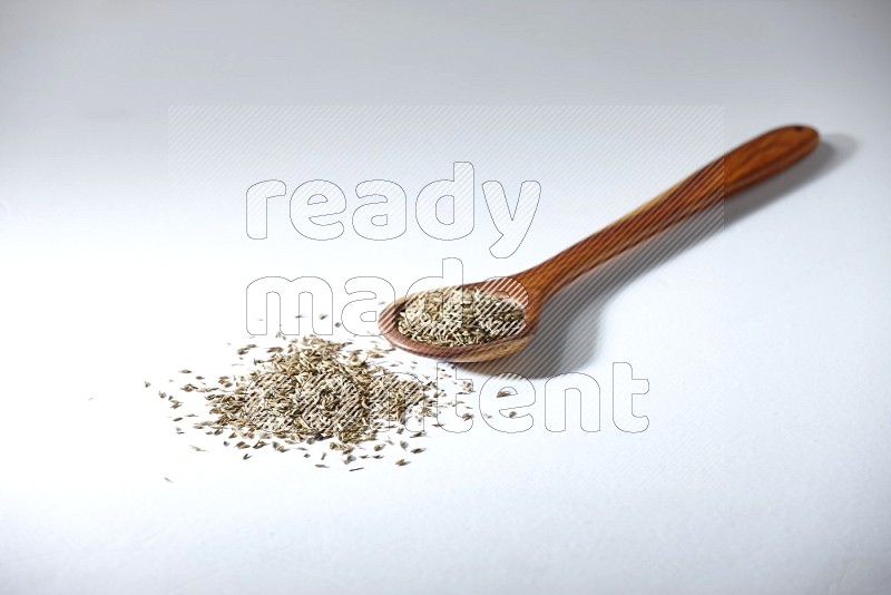 A wooden ladle full of cumin seeds on a white flooring