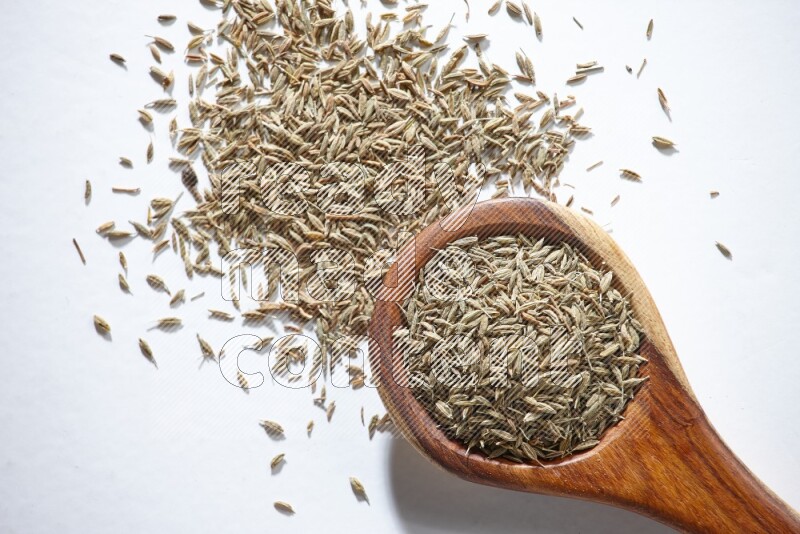 A wooden ladle full of cumin seeds on a white flooring