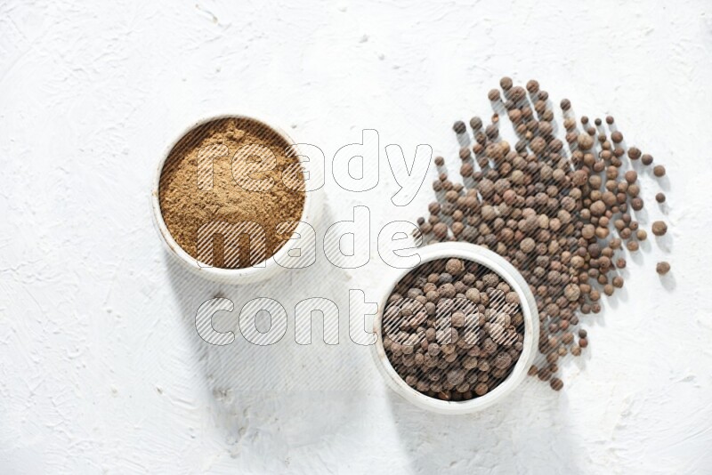 وعاءان بيج، أحدهما ممتلئ ببودرة بهار الفلفل الحلو والآخر بالحبوب مع البودرة والحبوب متناثرة على خلفية بيضاء