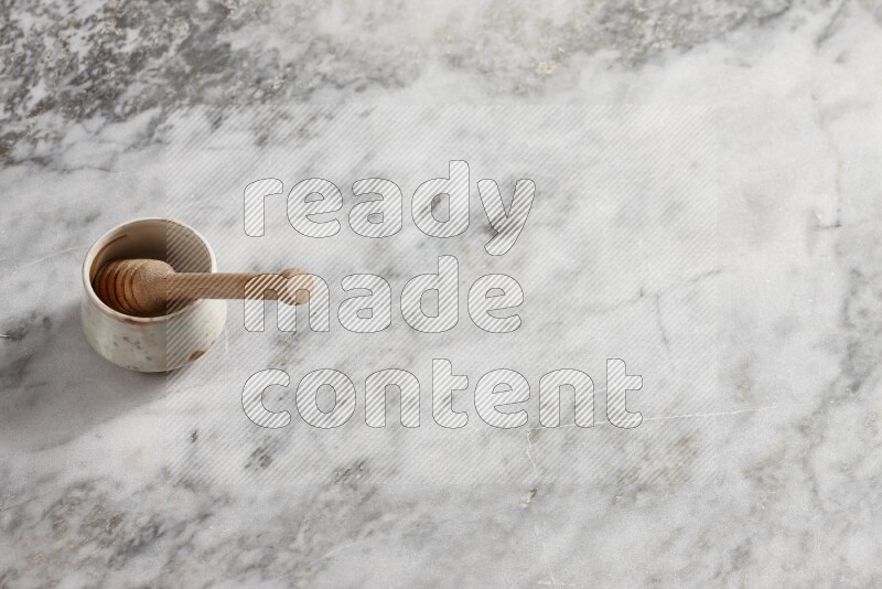 وعاء فخاري بيج مع ملعقة عسل خشبية بداخله على خلفية من الرخام الرمادي