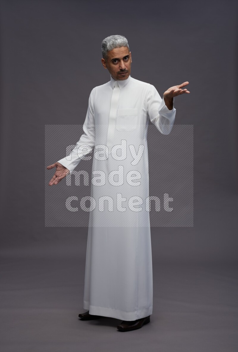 Saudi man wearing thob standing interacting with the camera on gray background