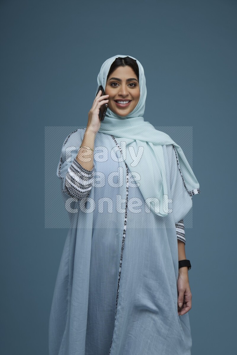 A Saudi woman having a Call in a blue background wearing blue Abaya with hijab