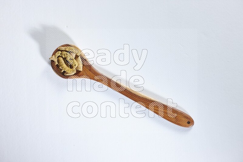 مغرفة خشبية مليئة بأصابع الكركم المجففة على خلفية بيضاء