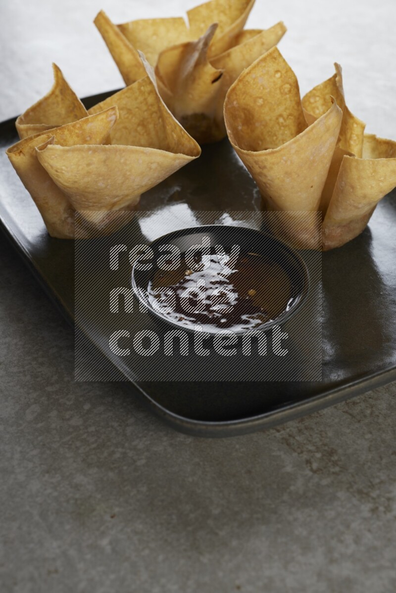 wonton cups with soy sauce ramkin on rectangle dark grey ceramic plate on grey textured counter top