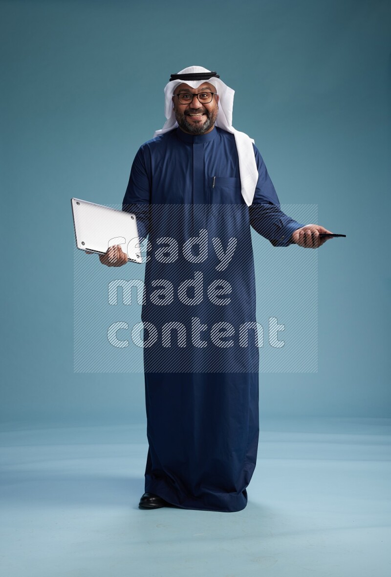 Saudi Man with shimag Standing texting on phone on blue background