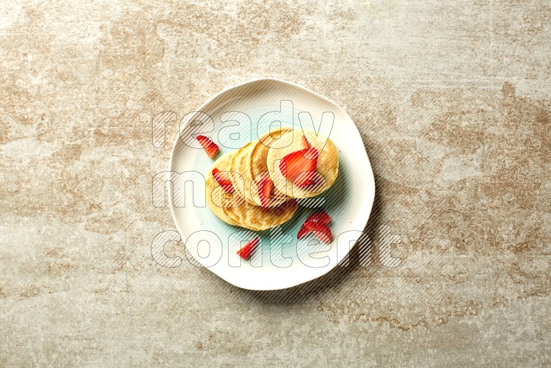 Five stacked strawberry mini pancakes in a bicolor plate on beige background