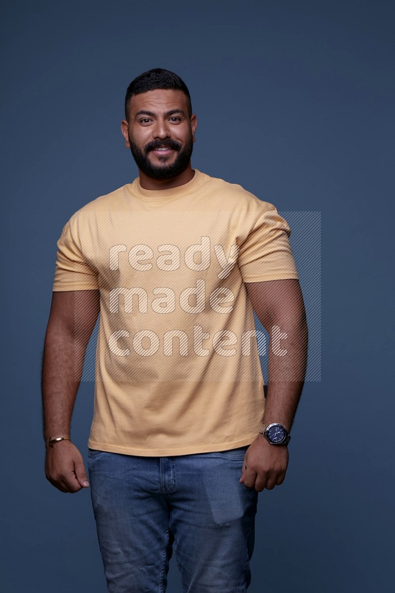 A man posing in a blue background wearing a yellow shirt