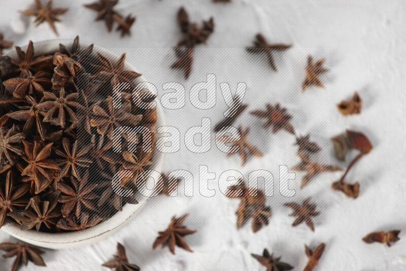 Star Anise in a white bowl and more of it sprinkled on white background