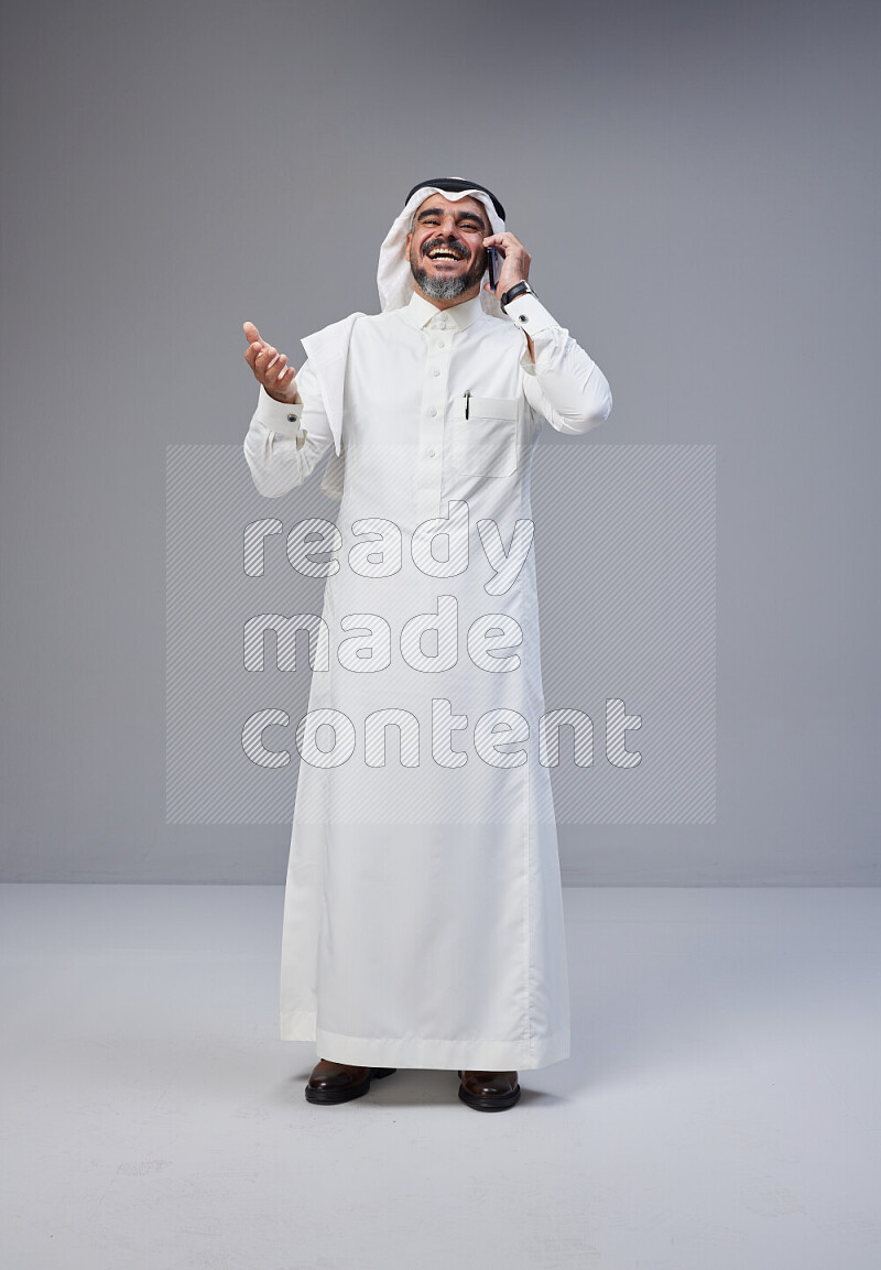 Saudi man Wearing Thob and white Shomag standing talking on phone on Gray background