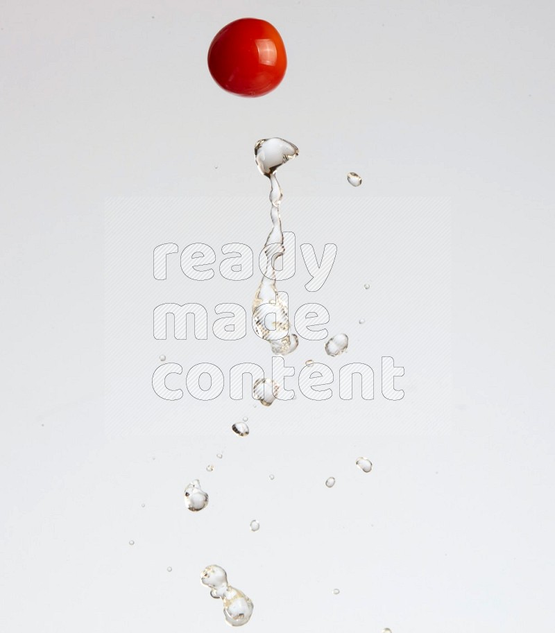 A single cherry tomato flying leaving a splash of water behind on a light blue background
