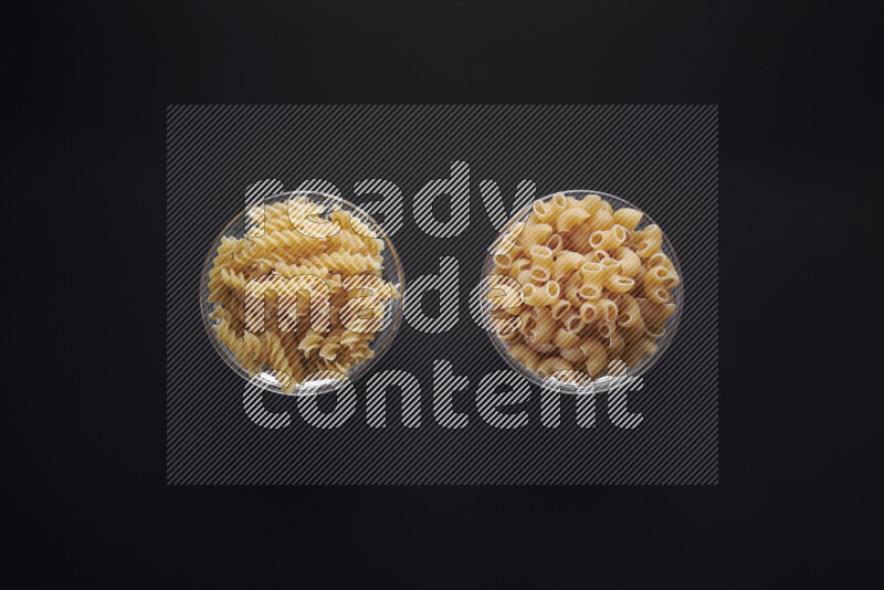 Different pasta types in glass bowls on black background