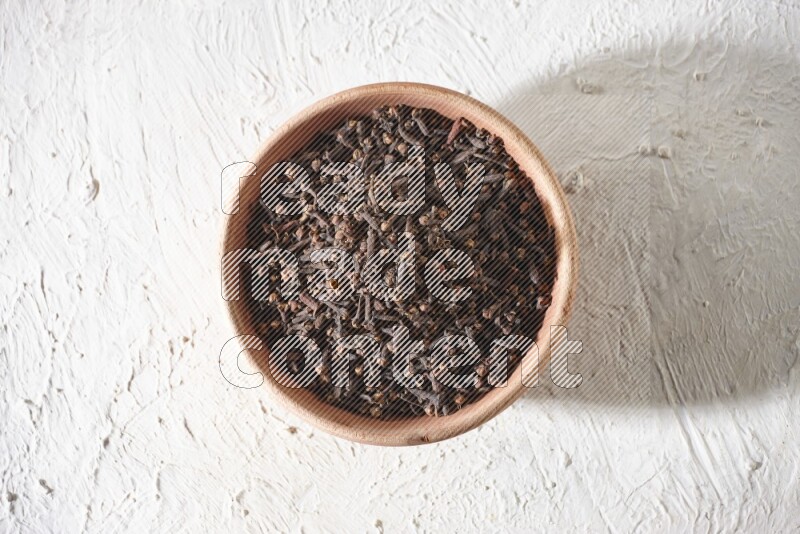 A wooden bowl full of cloves on a white flooring