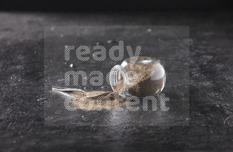 بودرة الفلفل الأسود في وعاء زجاجي مقلوب مع ملعقة معدنية مليئة بالبودرة علي خلفية سوداء