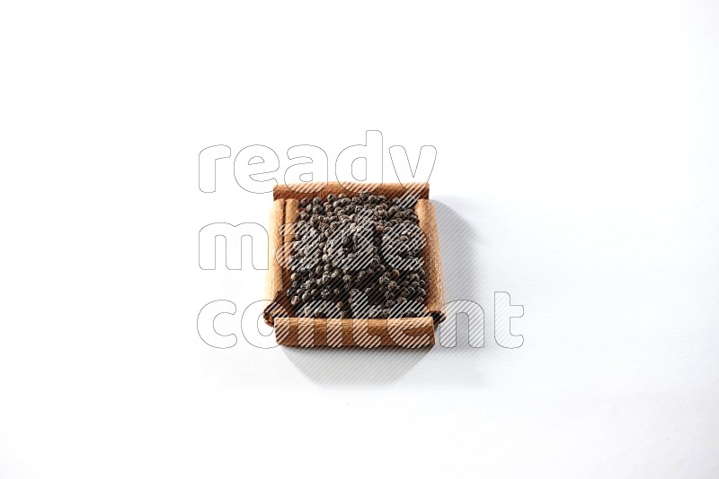 A single square of cinnamon sticks full of black pepper on white flooring