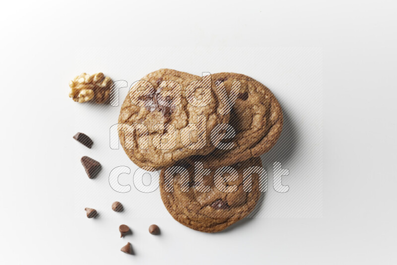 Chocolate chips cookies with chocolate and walnuts beside it on a white background