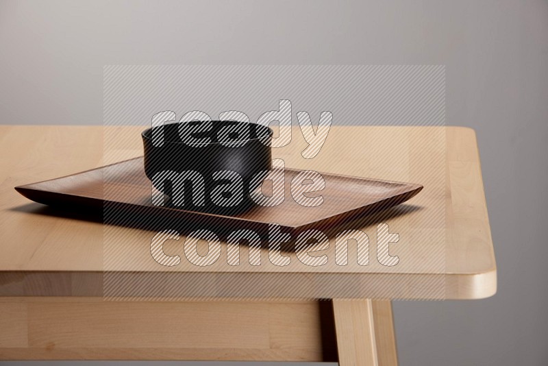 black bowl placed on a rectangular wooden tray on the edge of wooden table