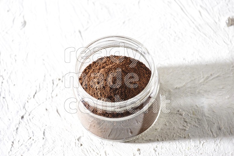 A glass jar full of cloves powder on a textured white flooring