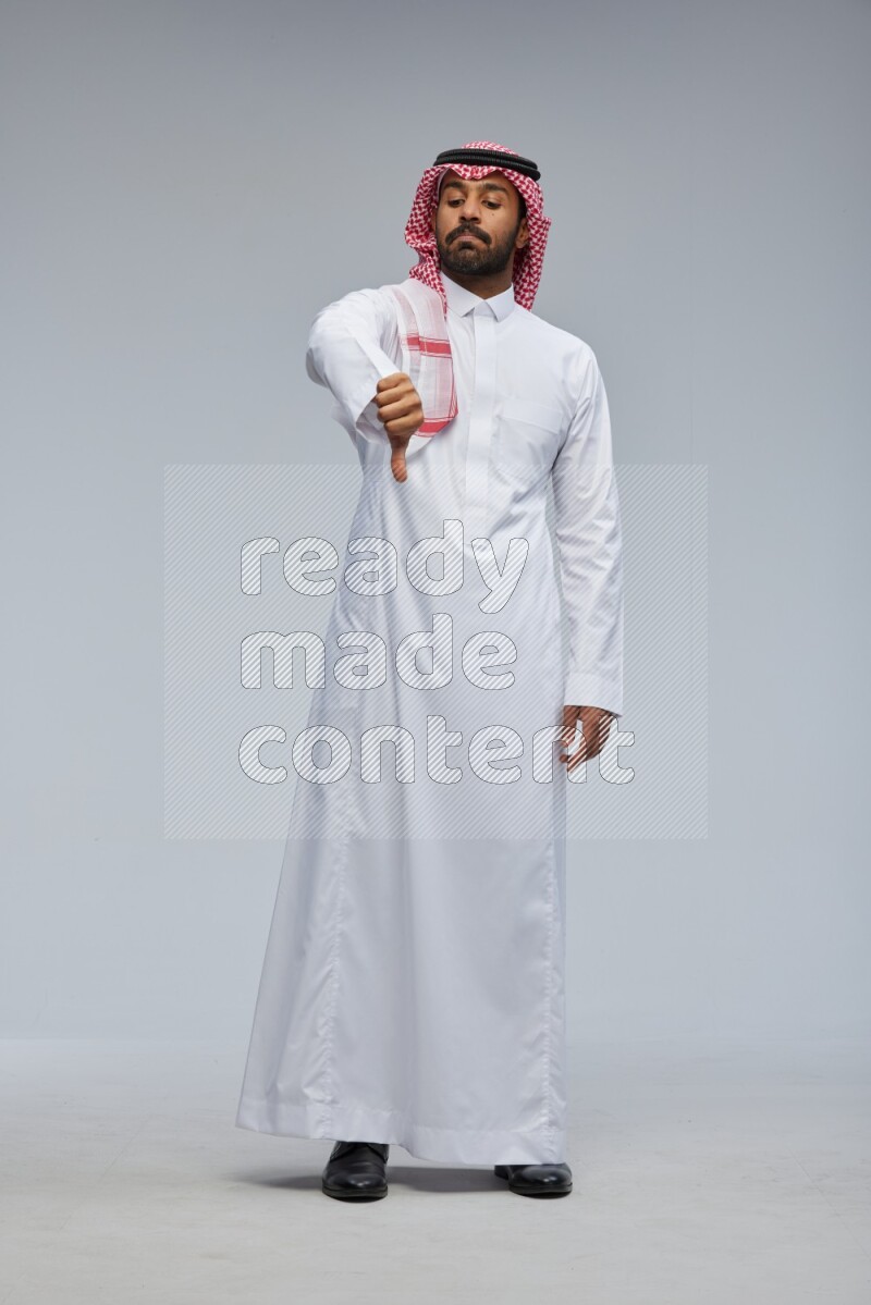 Saudi man Wearing Thob and shomag standing interacting with the camera on Gray background