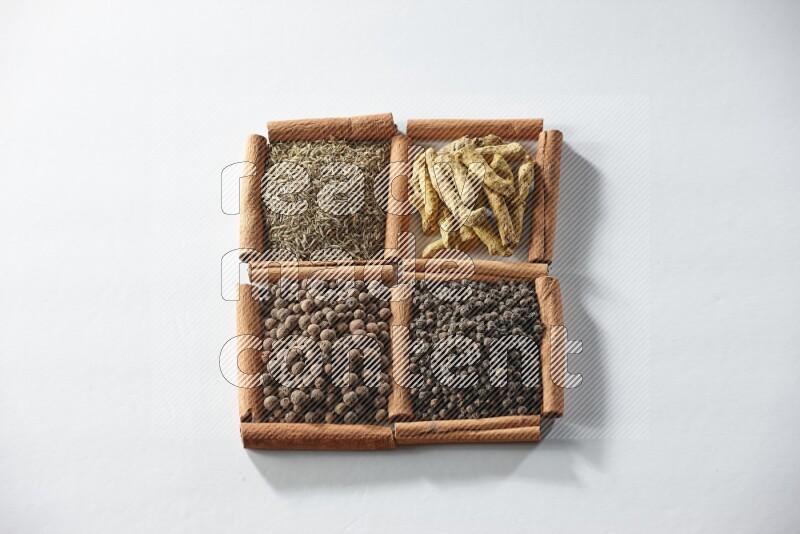 4 مربعات من أعواد القرفة ممتلئة بالكمون وأصابع الكركم وبهار الفلفل الحلو وحبوب الفلفل الأسود على أرضية بيضاء