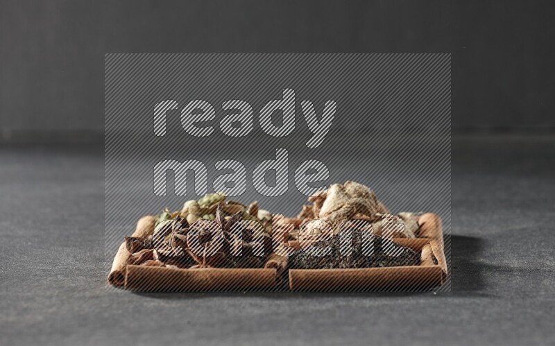 4 squares of cinnamon sticks full of tea, star anise, dried ginger and cardamom on black flooring