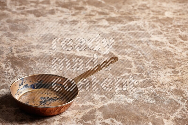 A small copper pan on beige marble background