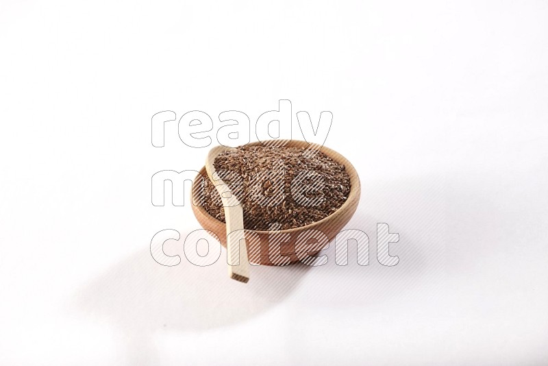 وعاء خشبي ممتلئ بحبوب بذر الكتان مع ملعقة خشبية ممتلئة بداخله علي خلفية بيضاء