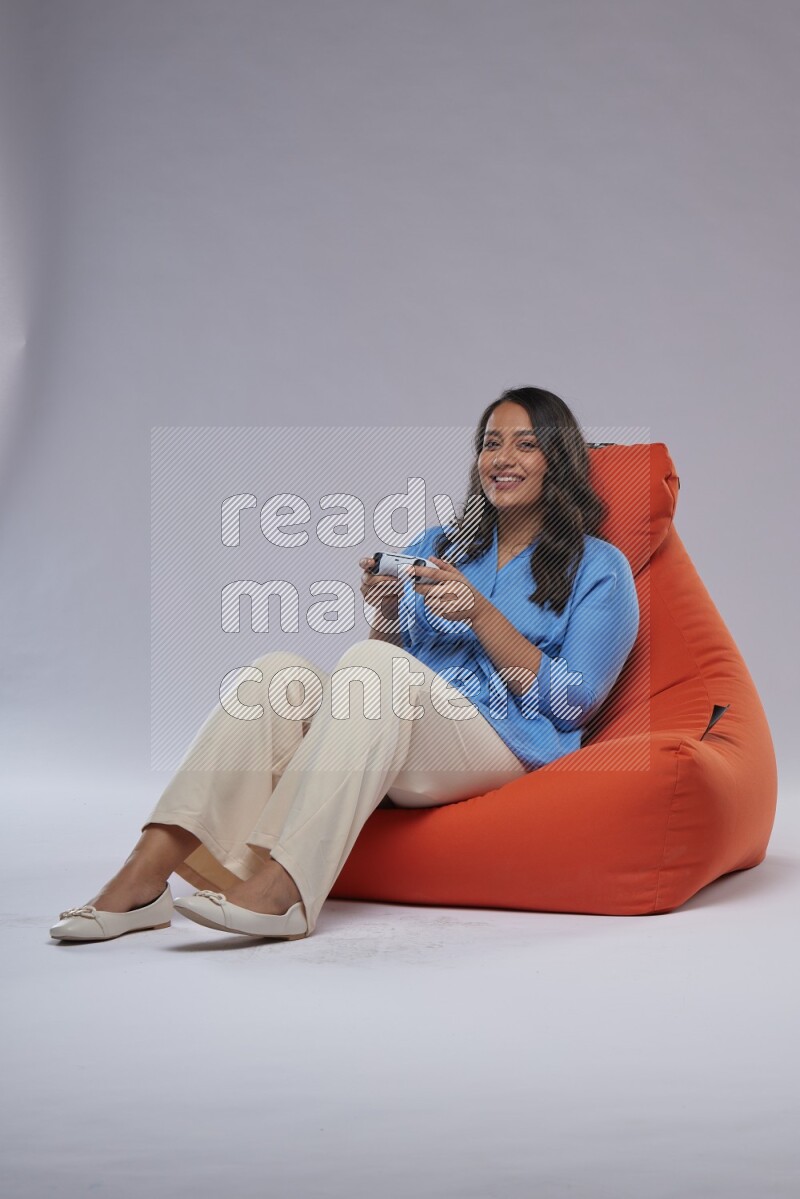A woman sitting on an orange beanbag and gaming with joystick