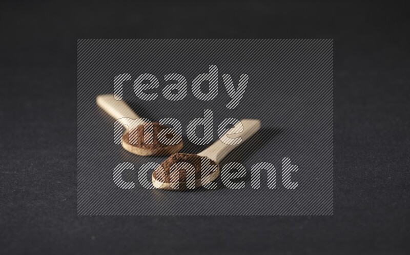 2 wooden spoons full of cloves powder on a black flooring