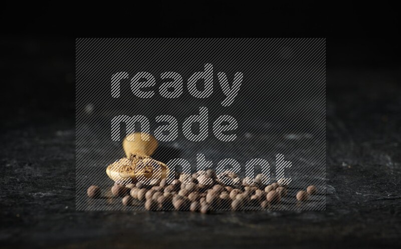 A wooden spoon full of allspice powder and whole balls spreaded on a textured black flooring