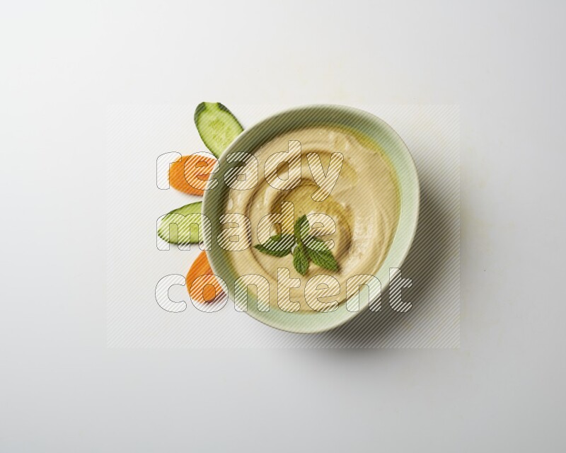 Hummus in a green plate garnished with mint on a white background