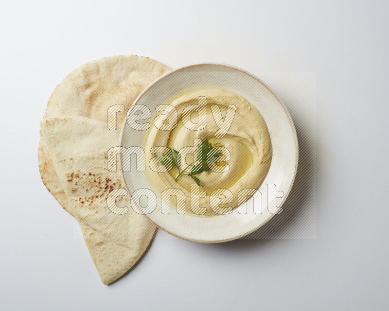Hummus in a pottry plate garnished with parsley on a white back ground