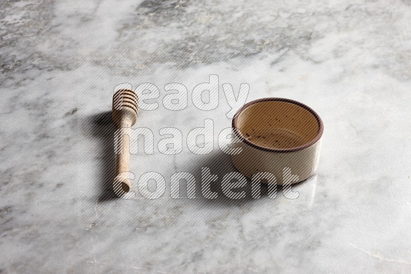 Beige Pottery Oven Bowl with wooden honey handle on the side with grey marble flooring, 45 degree angle