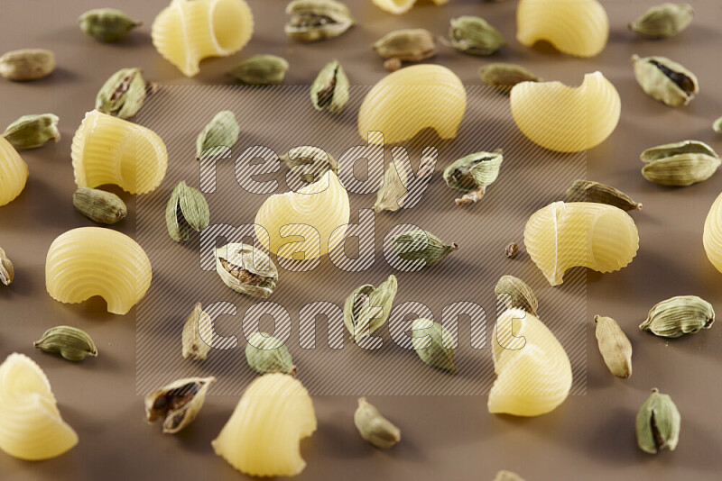 Raw pasta with different ingredients such as cherry tomatoes, garlic, onions, red chilis, black pepper, white pepper, bay laurel leaves, rosemary and cardamom on beige background