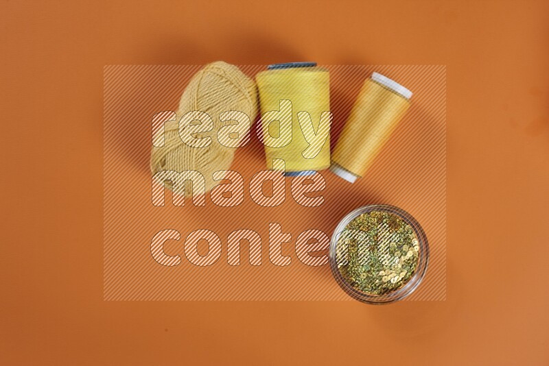 A yellow collection of sewing and tailoring tools arranged on a orange background