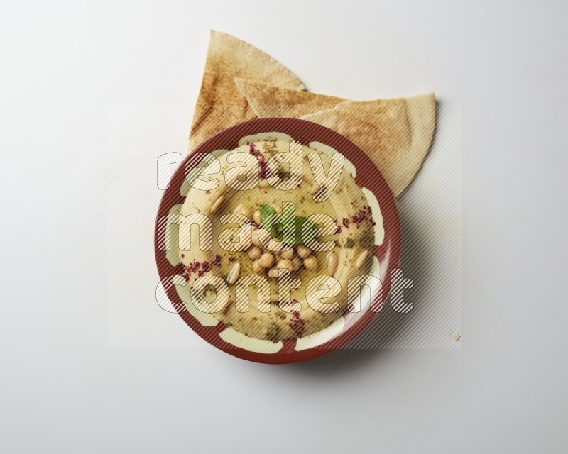 Hummus in a traditional plate garnished with zaatar & sumak on a white background