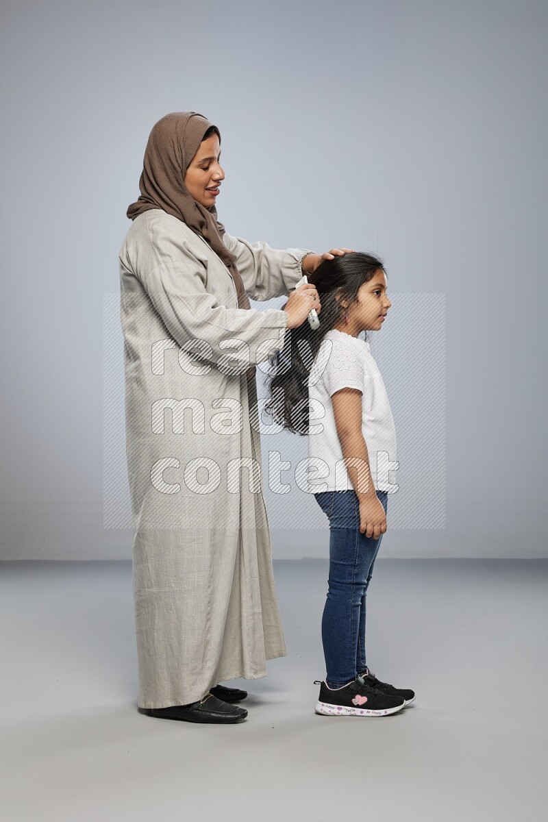 Mom standing styling hair for her daughter on gray background