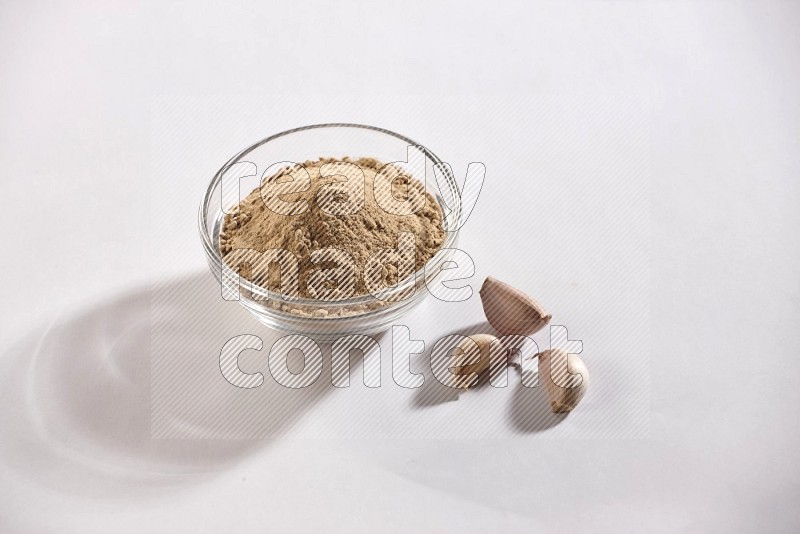 A glass bowl full of garlic powder and beside it garlic bulb and cloves on a white flooring in different angles