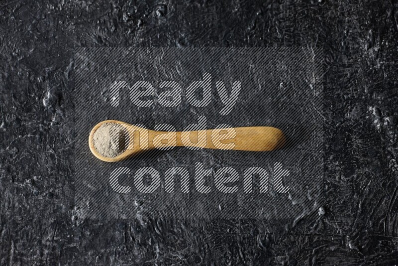 ملعقة خشبية مليئة ببودرة الفلفل الأبيض على أرضية سوداء